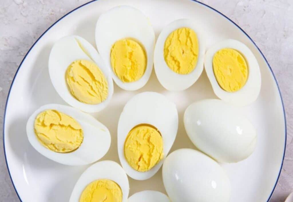 A plate containing several hard-boiled eggs, some cut in half to show the yellow yolks, on a light background.