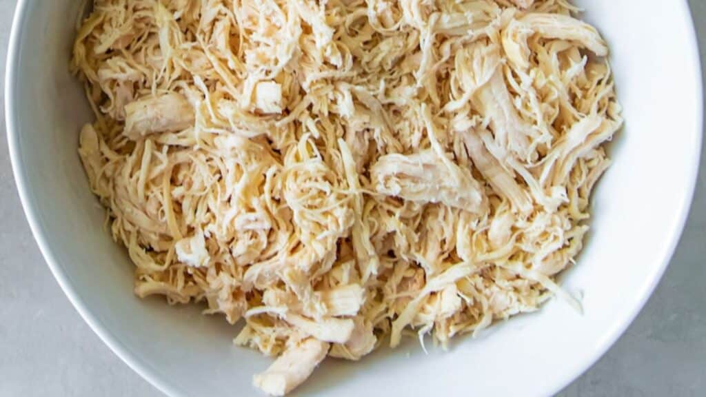 A bowl of shredded cooked chicken on a white surface.