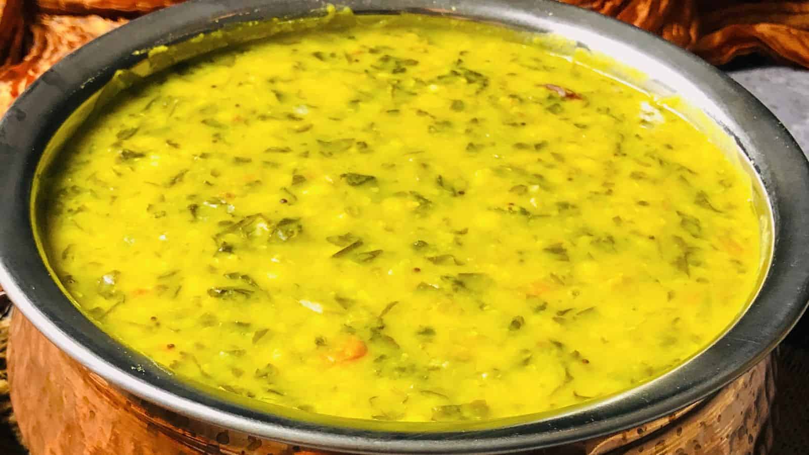 A close-up of a bowl of creamy, methi dal with visible spices and herbs.