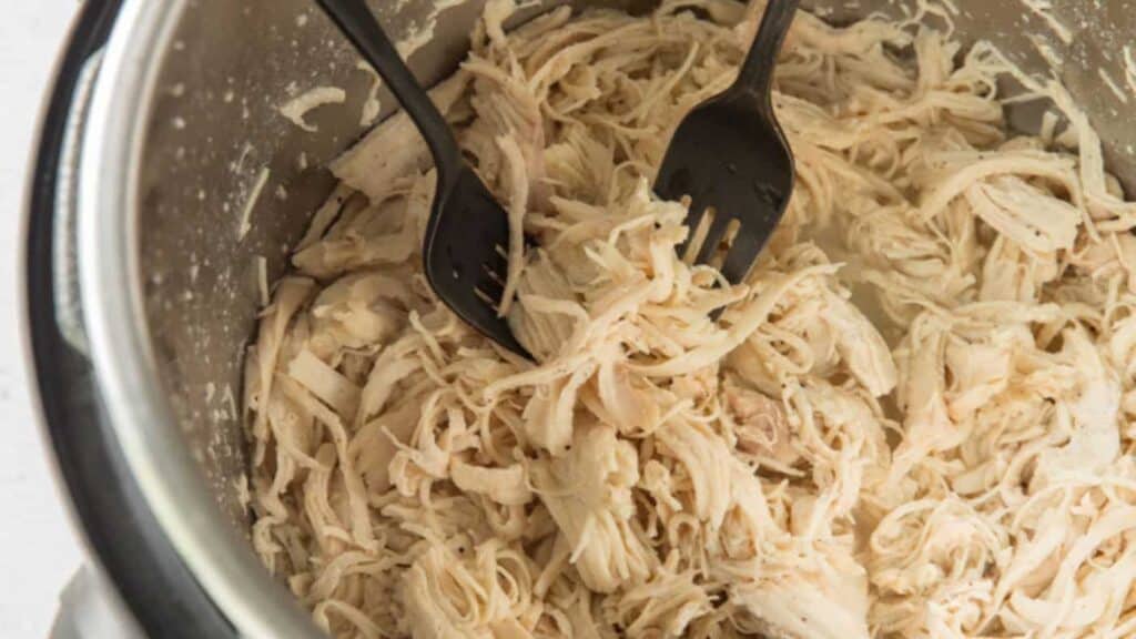 Shredded chicken in a metal bowl with two black forks.