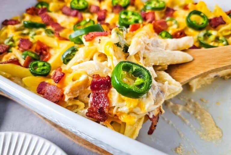 A casserole dish with creamy chicken pasta topped with bacon, melted cheese, and sliced jalapeños.