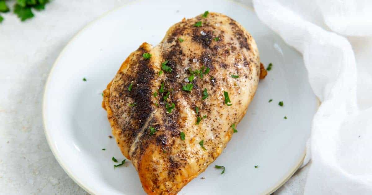 Juicy Air Fryer Boneless Skinless Chicken Breast on a white plate with parsley, onions, and tomatoes.