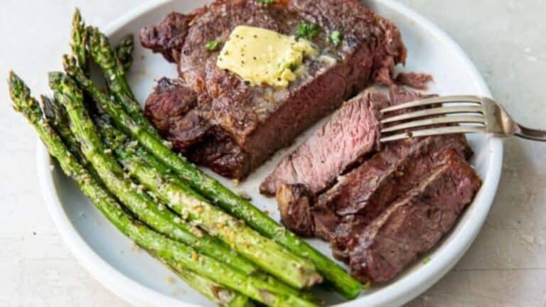 air fryer medium rare ribeye sliced on a plate with asparagus and a fork.