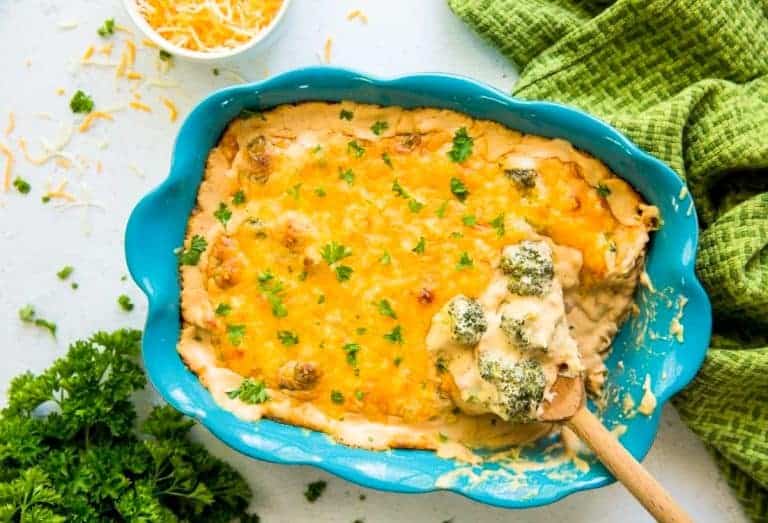 Keto Broccoli Cheese Casserole in a blue casserole dish with parsley and a wooden spoon.