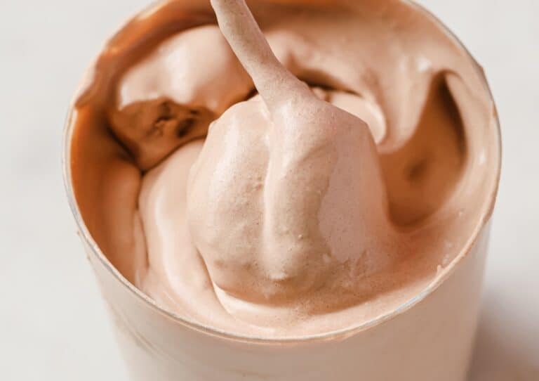 Close-up of a creamy chocolate soft serve ice cream in a white cup.
