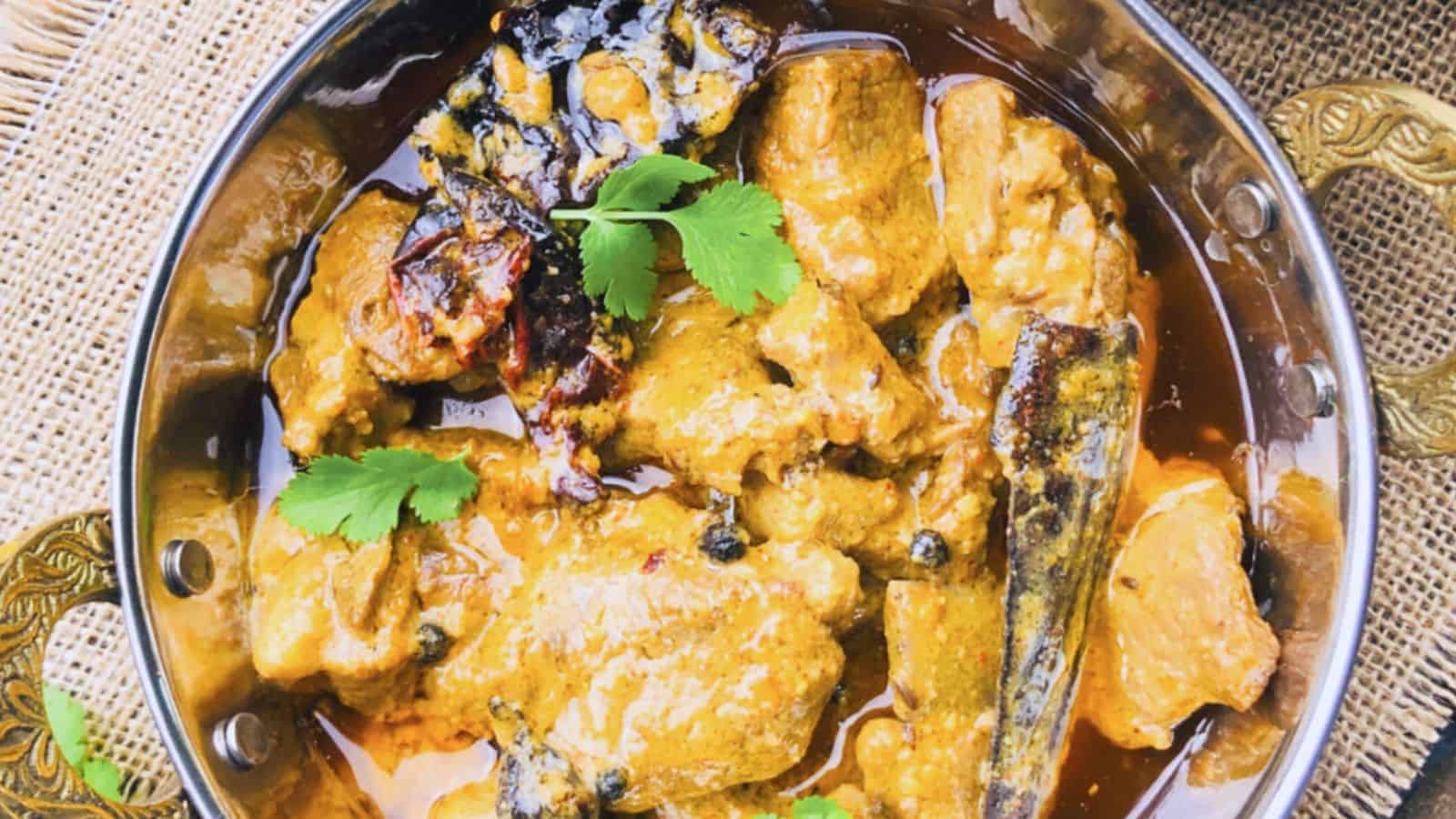 A bowl of Lamb Rogan Josh, garnished with cilantro and served in a decorative brass dish.