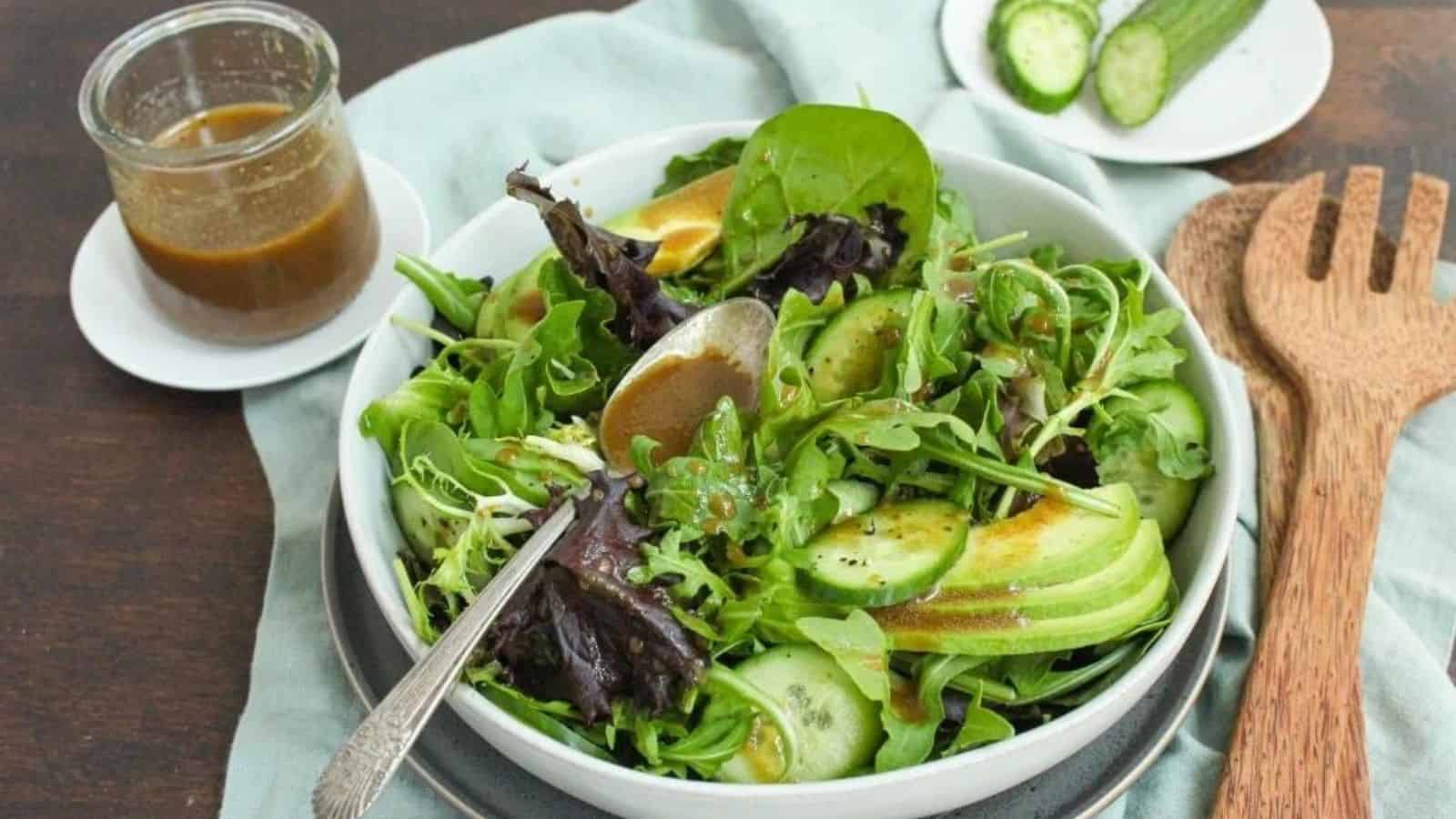 A green salad tossed with balsamic dressing in a white bowl with a jar of salad dressing beside it.