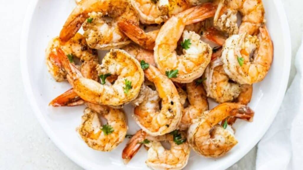 A plate of seasoned, grilled shrimp garnished with parsley on a white background.
