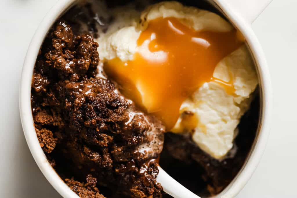 Close-up of a dessert in a white bowl featuring warm chocolate cake, vanilla ice cream, and caramel sauce.