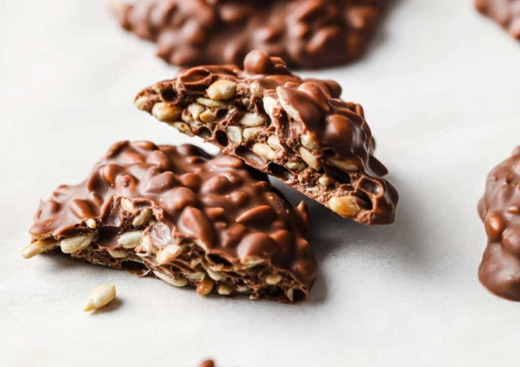 Pieces of chocolate bark with sunflower seeds, crisply broken, displayed on a light surface.