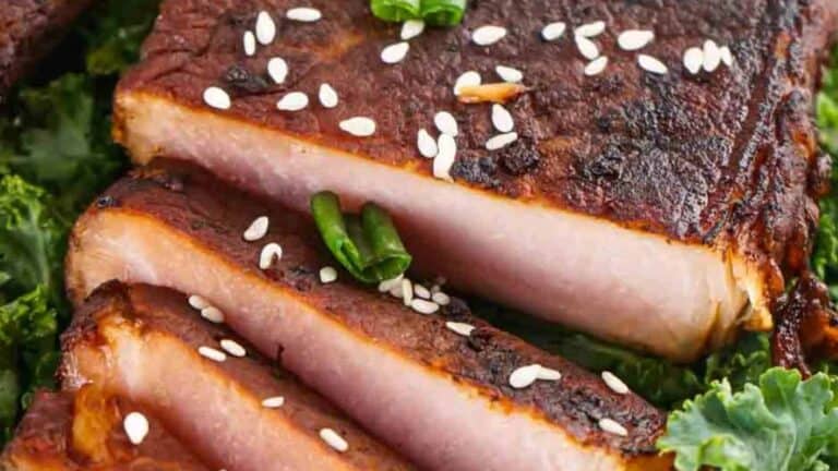 Close-up of sliced grilled pork belly with sesame seeds on top, served on a bed of kale.