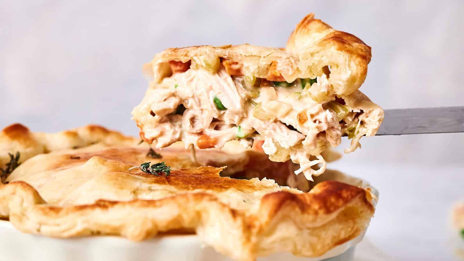 A slice of chicken pot pie being lifted, showing its creamy filling with chunks of chicken and vegetables, garnished with thyme.