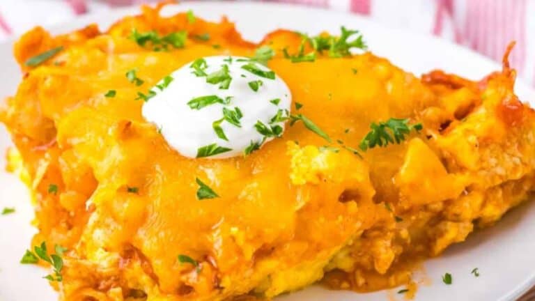 A serving of chicken tamale pie topped with a dollop of sour cream and garnished with chopped herbs on a white plate.