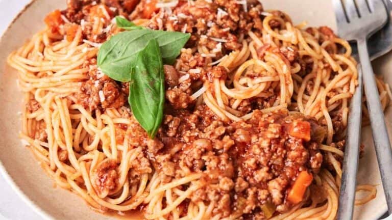 A plate of spaghetti topped with a meaty tomato sauce and a fresh basil leaf, served with a fork on the side.