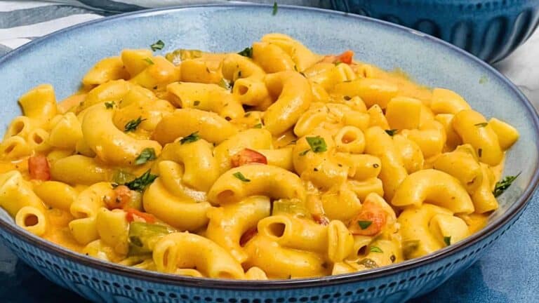 A bowl of creamy Masala Mac and Cheese with chopped herbs, served in a blue dish.