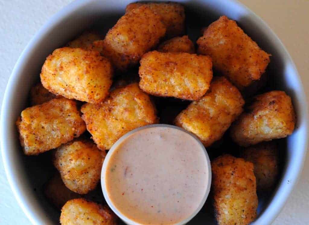 A bowl of crispy tater tots served with a side of dipping sauce, leaving you asking for seconds.