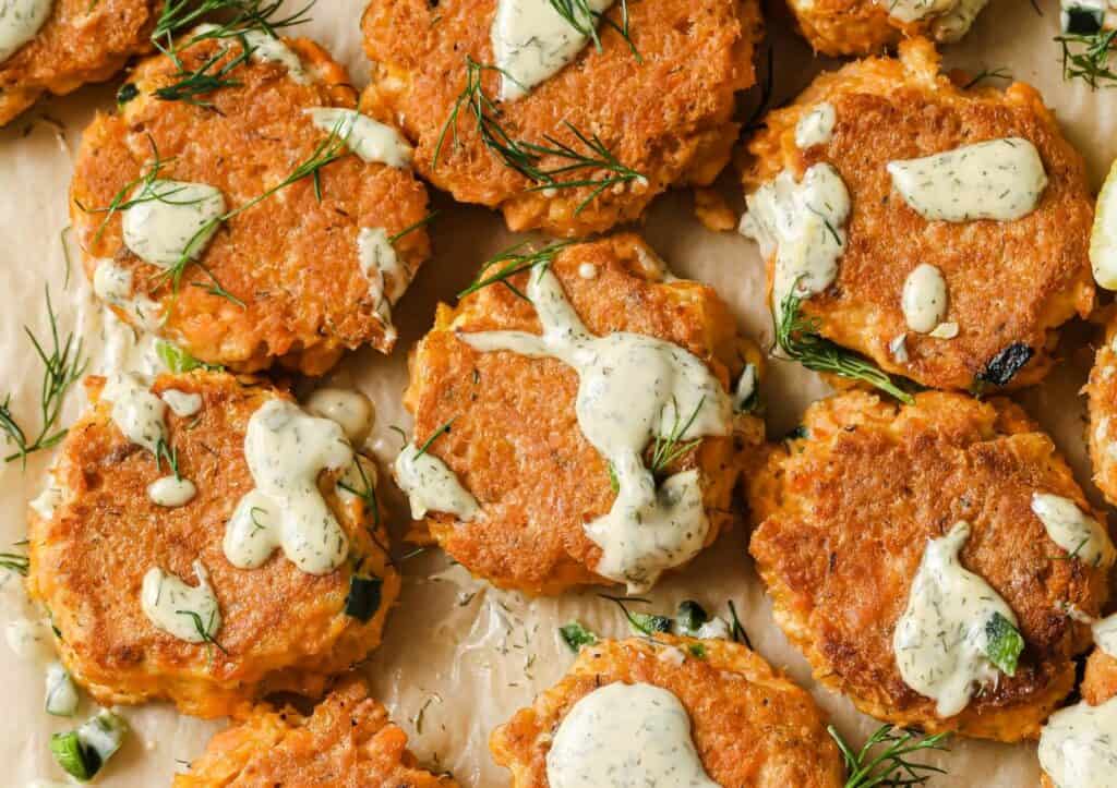 Close-up of golden brown salmon patties topped with dill sauce on a serving tray.