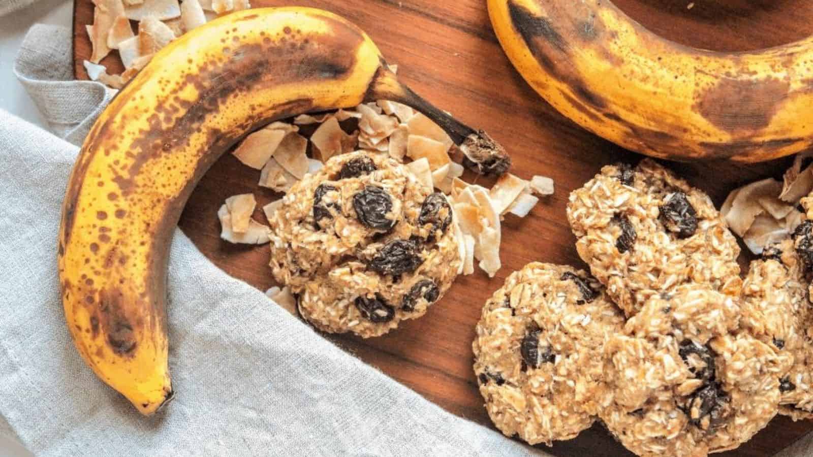 A wooden platter with oatmeal raisin cookies next to a banana.