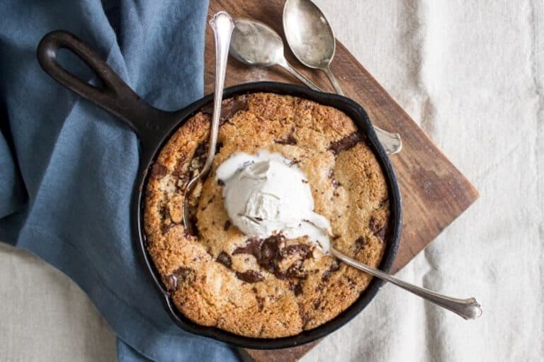 Freshly baked skillet cookie topped with a scoop of ice cream, served with spoons ready for sharing.
