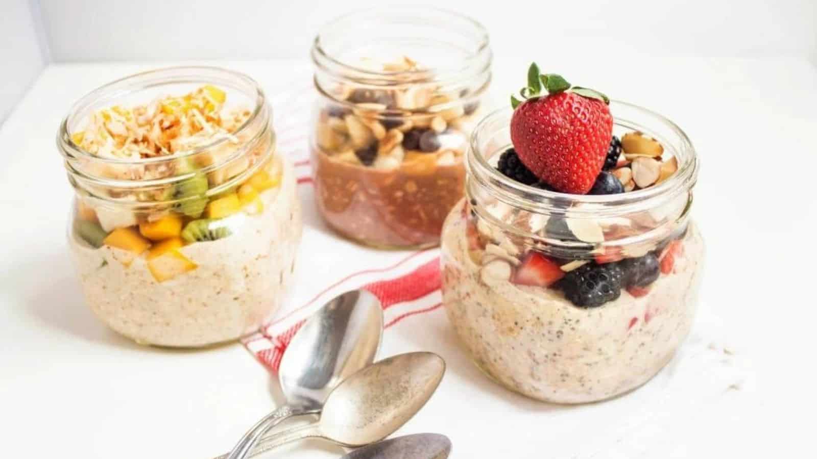 Three jars of overnight oats with different toppings like berries, shredded coconut, chopped banana, and almonds.