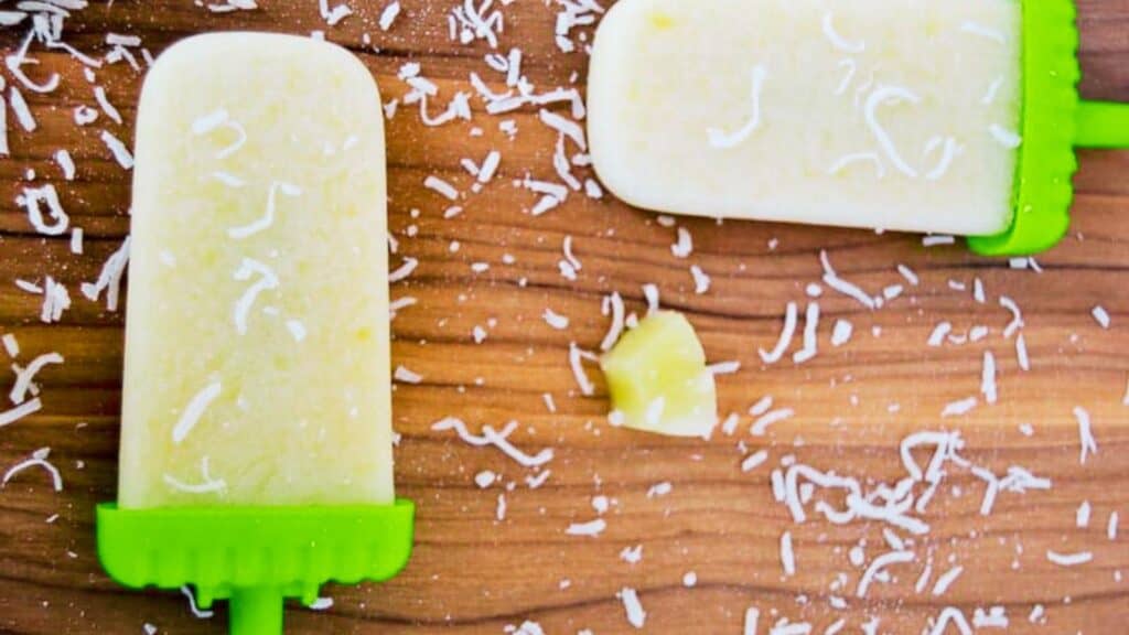 A homemade coconut popsicle on a wooden surface, with sprinkled coconut flakes.