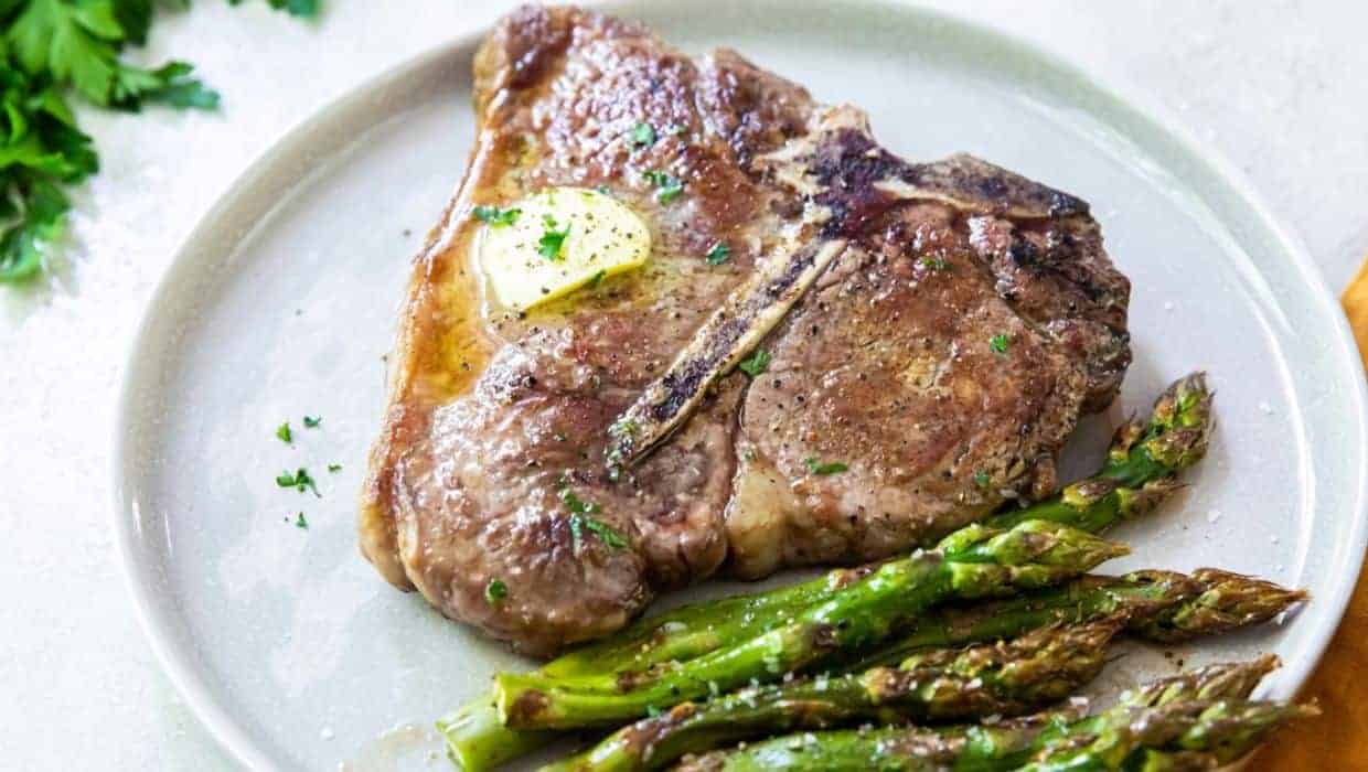 Seared Porterhouse Steak with butter, parsley, and asparagus on a white plate.