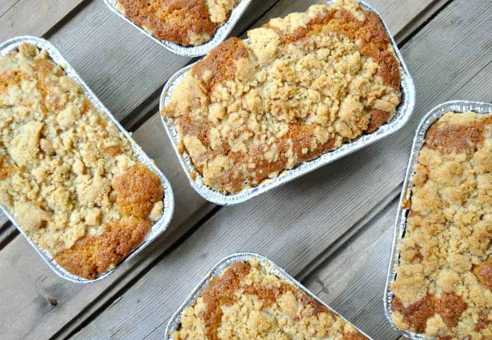 Five mini loaf pans of freshly baked crumb cake arranged on a wooden surface.