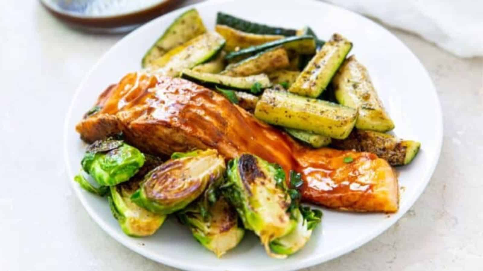 Salmon on the Blackstone Griddle with brussel sprouts and zucchini on a white plate.