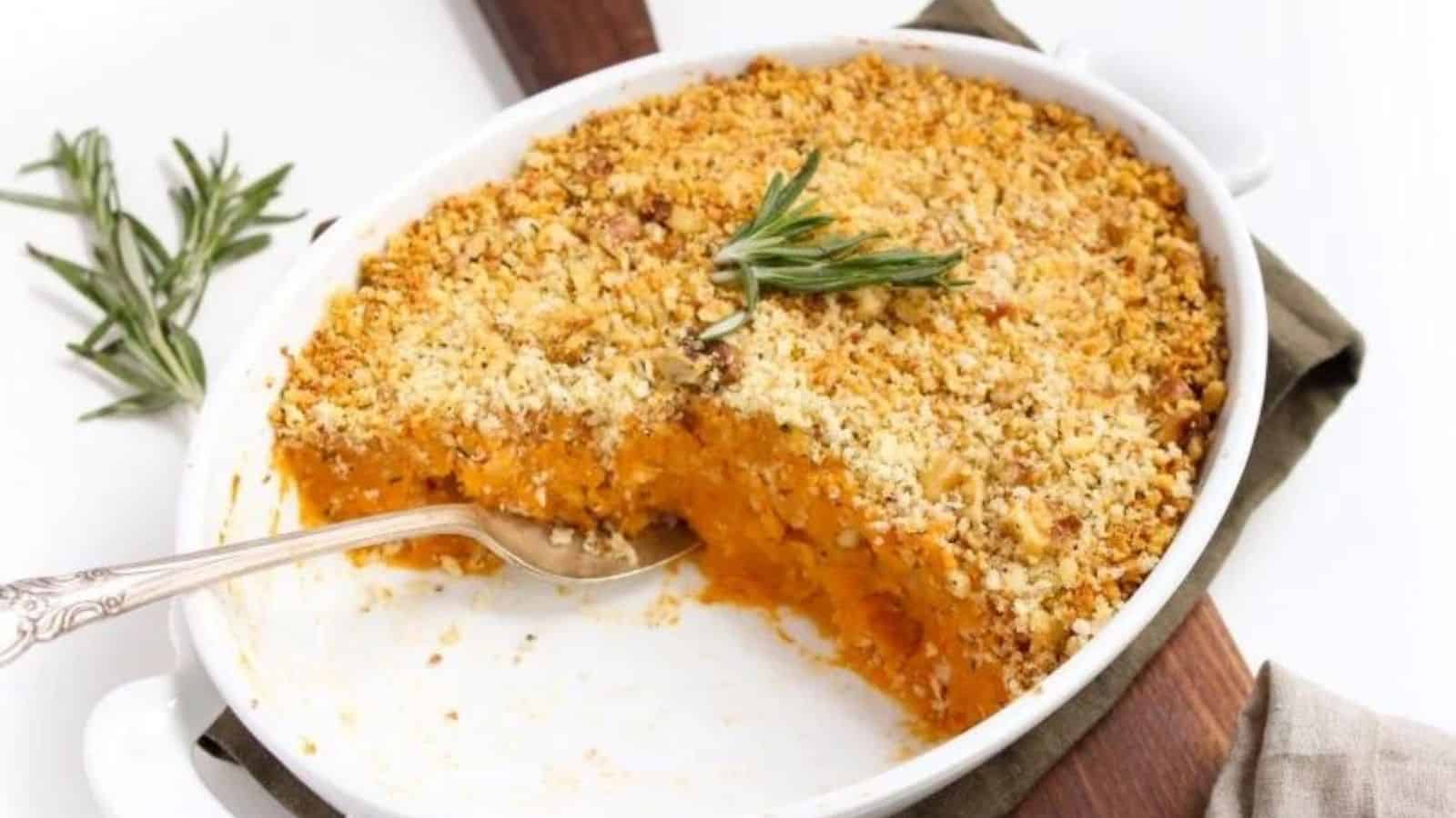 A white casserole dish halfway filled with sweet potato casserole topped with golden breadcrumbs and crushed nuts.