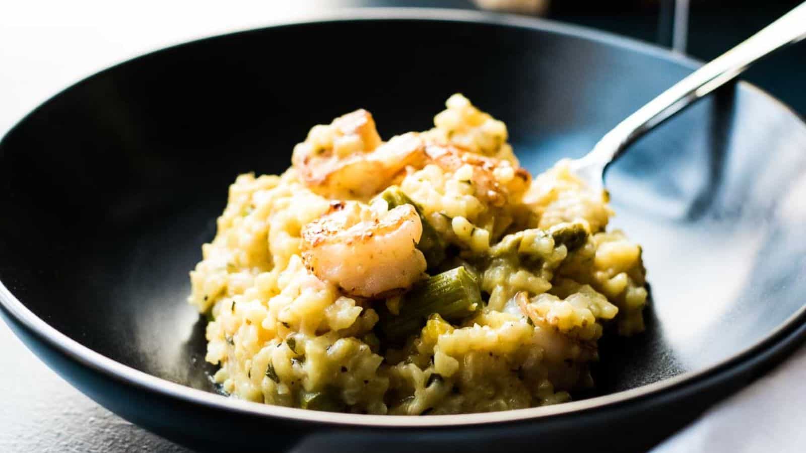 Shrimp asparagus risotto in a dark bowl on a blue background with a napkin and glass of wine.