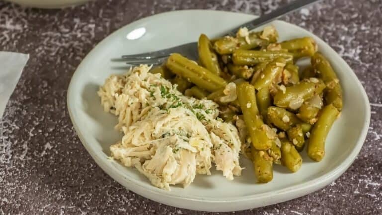 A plate of shredded chicken and seasoned green beans, garnished with herbs, served with a fork on the side.