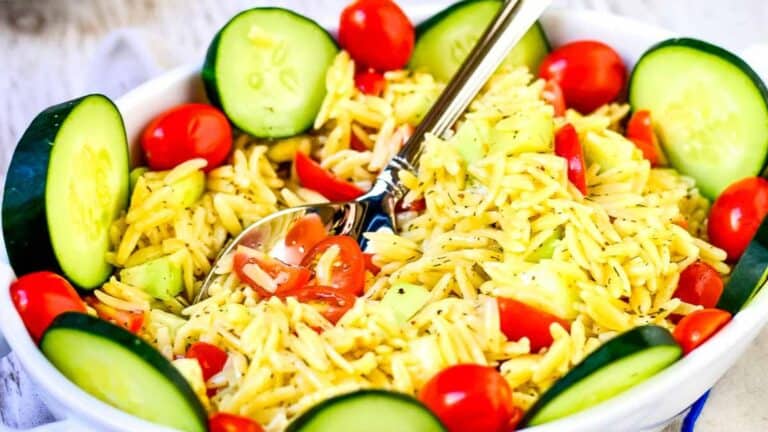 A bowl of orzo pasta salad with cherry tomatoes and cucumber slices.