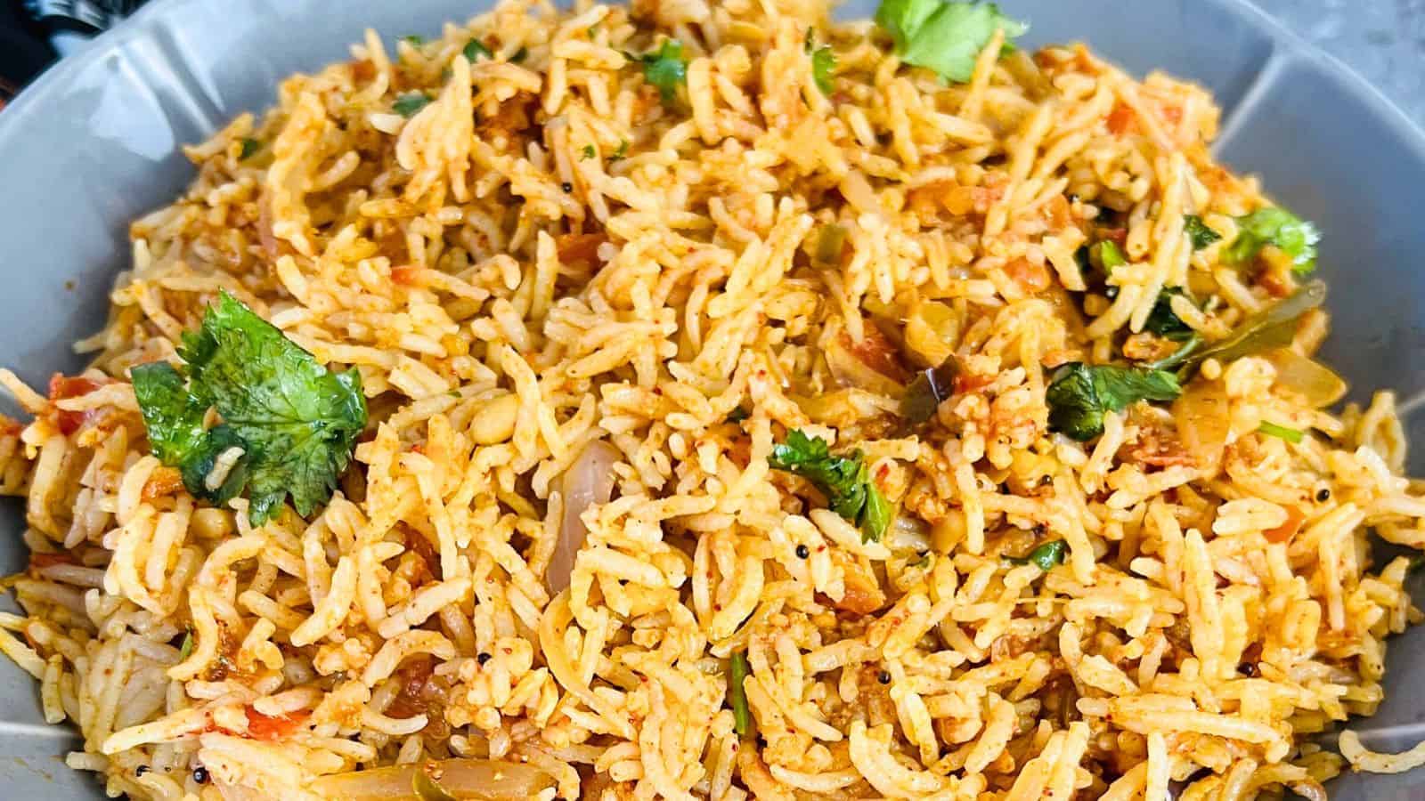 A close-up of a dish of Tomato Rice with fresh cilantro leaves in a blue bowl.