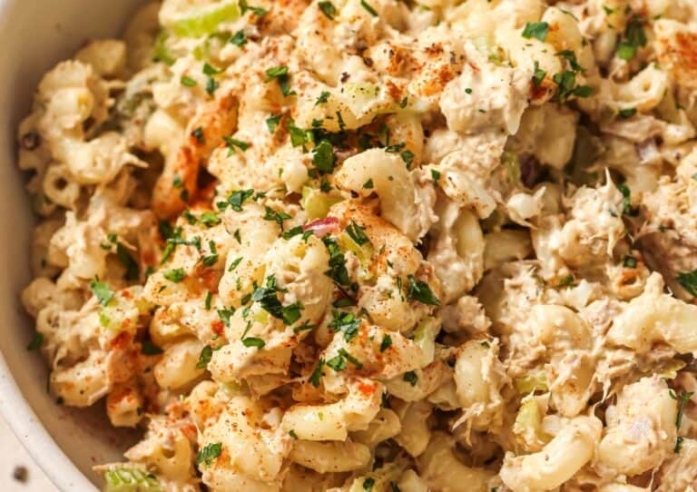 Close-up of a creamy pasta salad sprinkled with paprika and garnished with chopped herbs in a white bowl.