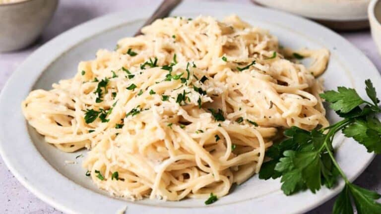 A plate of creamy fettuccine alfredo garnished with chopped parsley, served on a gray plate.