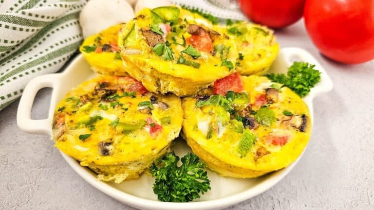 A plate of colorful vegetable mini frittatas served on a table with tomatoes on the side.