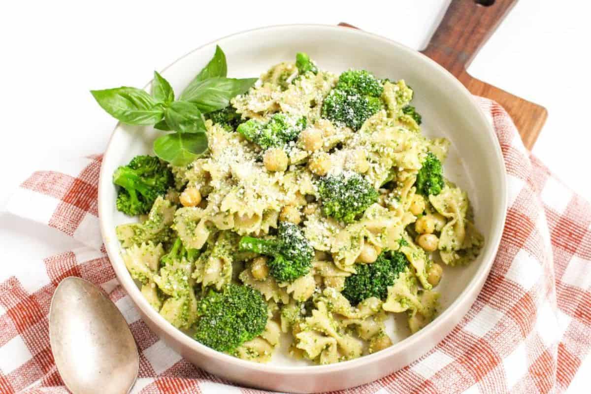 A shallow white bowl filled with pasta, broccoli, and chickpeas tossed in green pesto sauce.