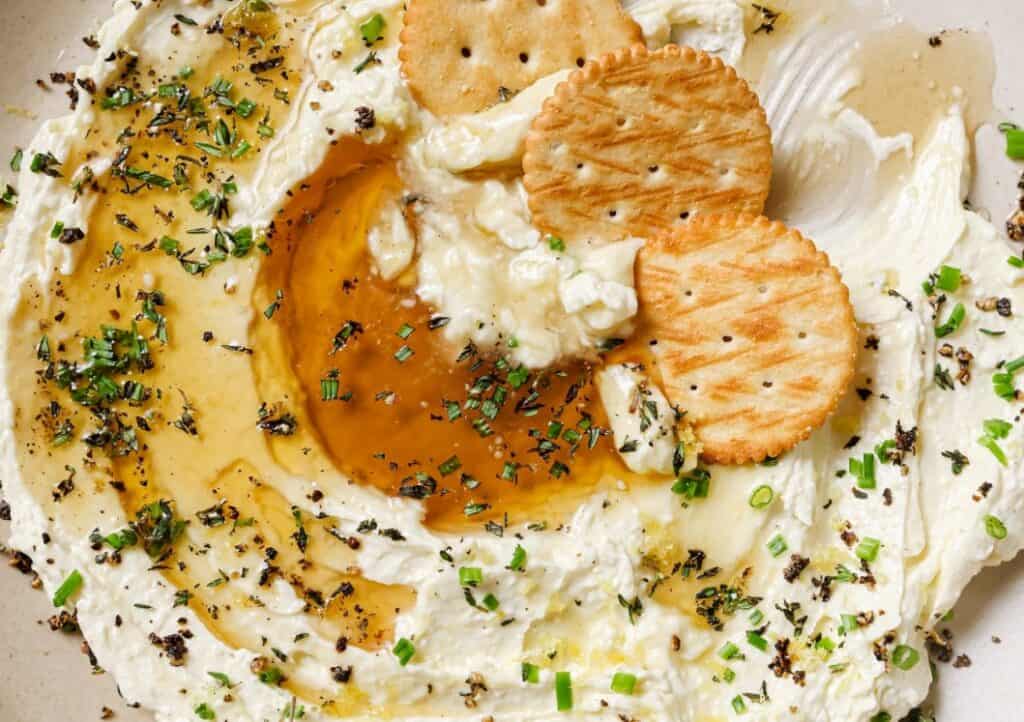 Plate of creamy dip topped with olive oil, herbs, and crackers.