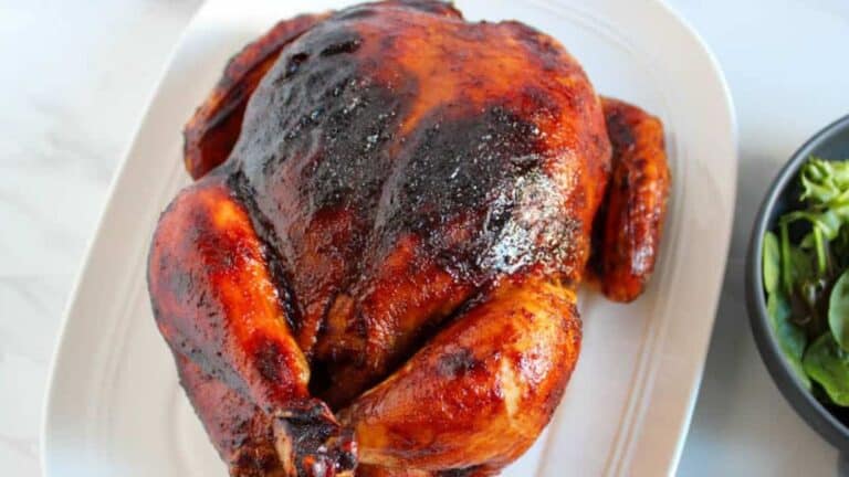 Roasted chicken with crispy, golden-brown skin served on a white oval platter, accompanied by a side of green salad in a black bowl.