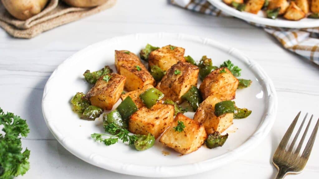Roasted diced potatoes and green bell peppers garnished with parsley on a white plate.