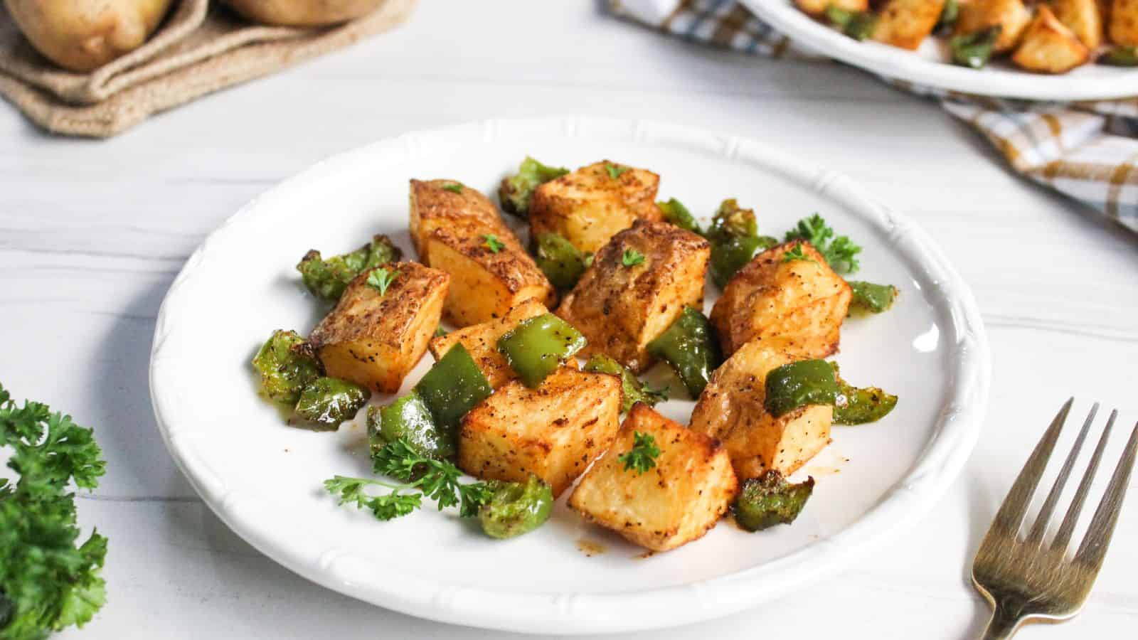 Air-fried potato cubes with diced green bell peppers on plate.