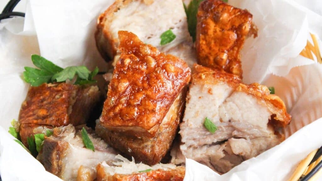 A basket of crispy roasted pork belly pieces garnished with fresh parsley.