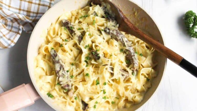 Alfredo steak pasta in skillet with wooden spoon.