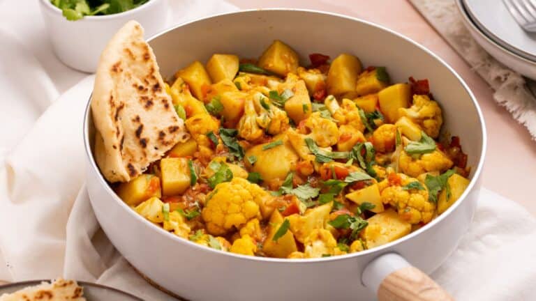 Vegetable curry with potatoes and cauliflower served in a pan with a side of flatbread.