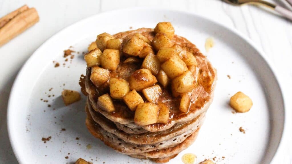 Stack of pancakes topped with cinnamon-spiced apple chunks on a white plate.