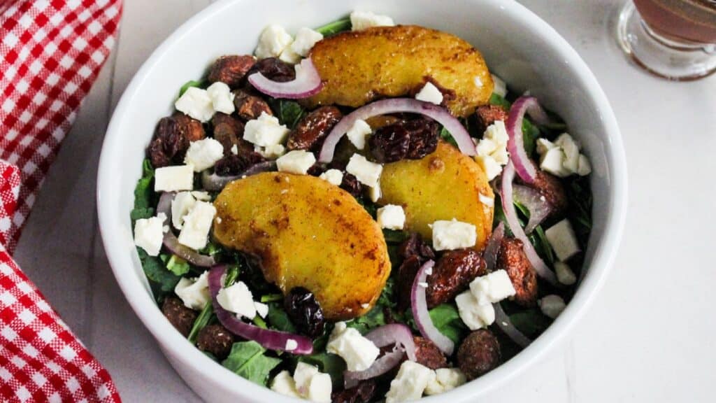 A bowl of salad with mixed greens, air-fried apples, red onions, nuts, and crumbled cheese.