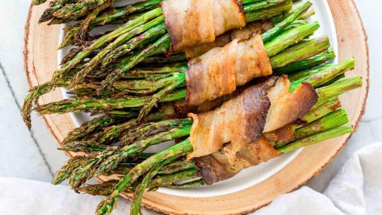 Roasted asparagus wrapped in bacon served on a ceramic plate.