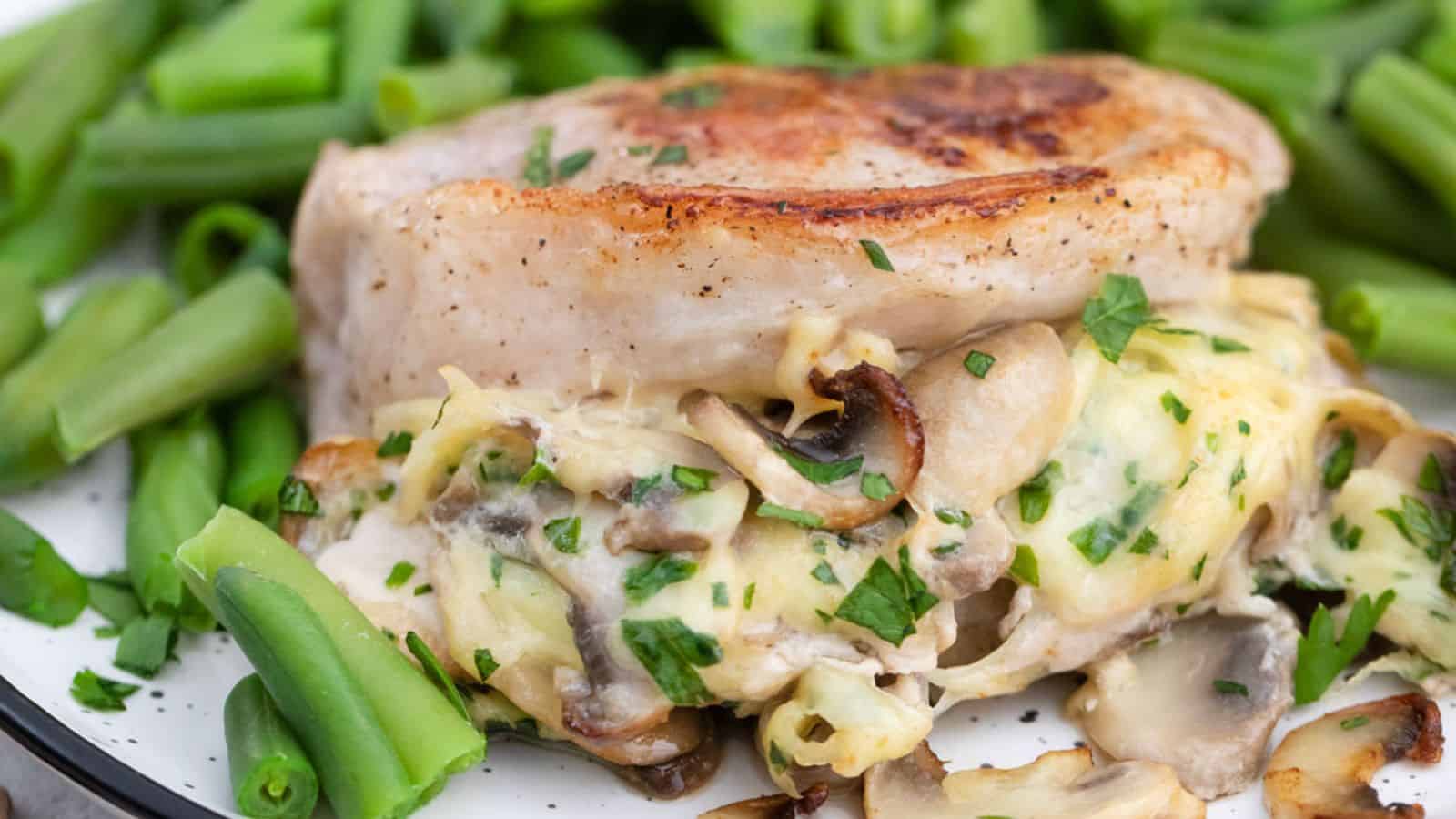 A plate of pork chops stuffed with mushrooms and cheese served with green beans.