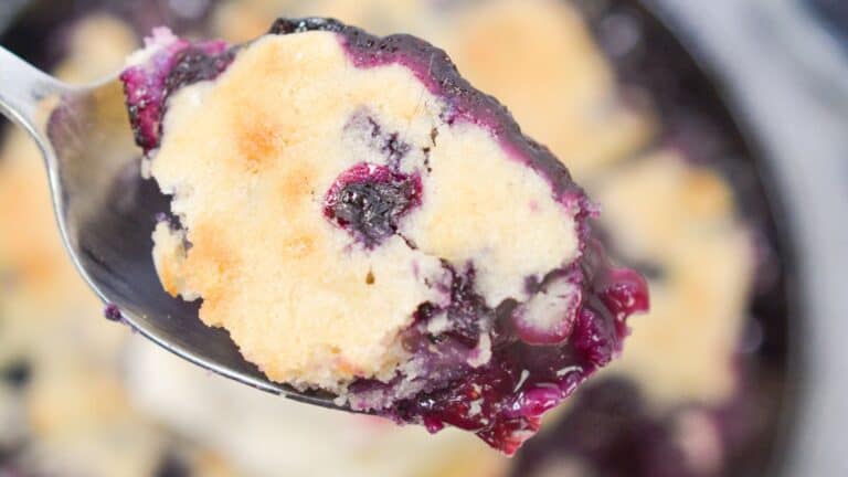 A spoon with blueberry cobbler with rest of cobbler in background.