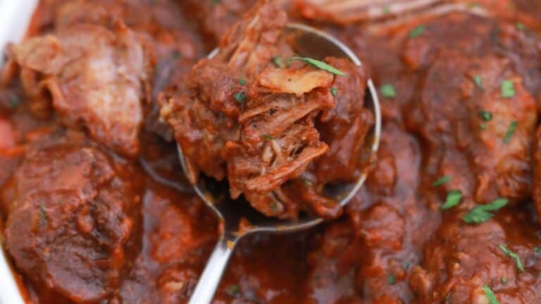 A close-up of braised short ribs in a tomato-based sauce, garnished with herbs.